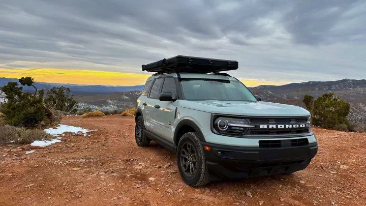 A light grey Bronco Sport SUV with rooftop tent on a dirt trail. Ideal RV rental for mountain adventures at sunset.. Ford Bronco Sport 2022