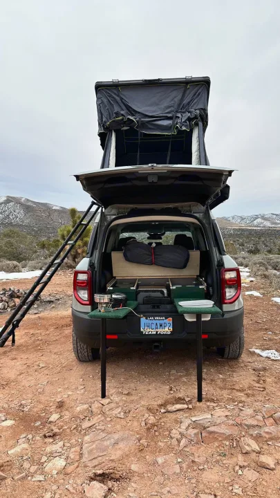 Explore with this Ford Bronco Sport rv rental, featuring a deployed rooftop tent, rear kitchen setup, and ladder in a snowy desert.. Ford Bronco Sport 2022