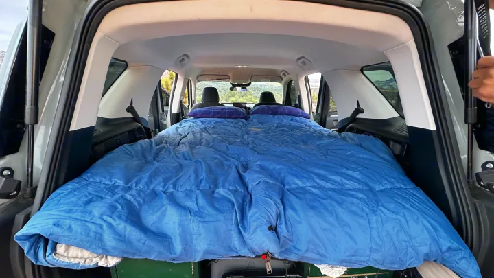 Vehicle's spacious rear transformed into a bed with blue bedding, ideal for an RV rental or car camping adventure.. Ford Bronco Sport 2022