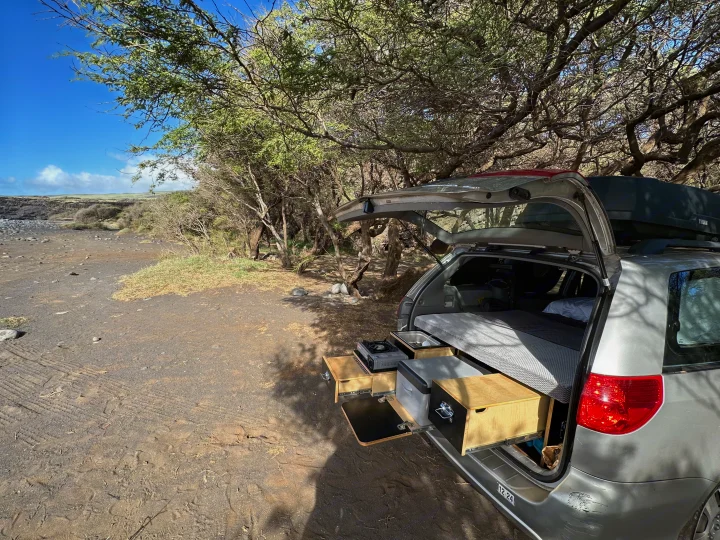 Grey car, configured like an RV rental, with a pull-out kitchen & bed setup for overlanding in a coastal area.. Toyota Other 2006