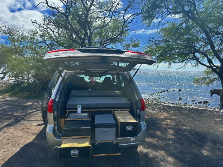 Gray SUV RV rental by the ocean, showing its rear converted into a camper with a bed, sink, and cooler drawers.. Toyota Other 2006