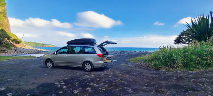 Coastal adventure with an rv rental minivan! Parked on a dark beach, tailgate open with pull-out kitchen visible.. Toyota Other 2006
