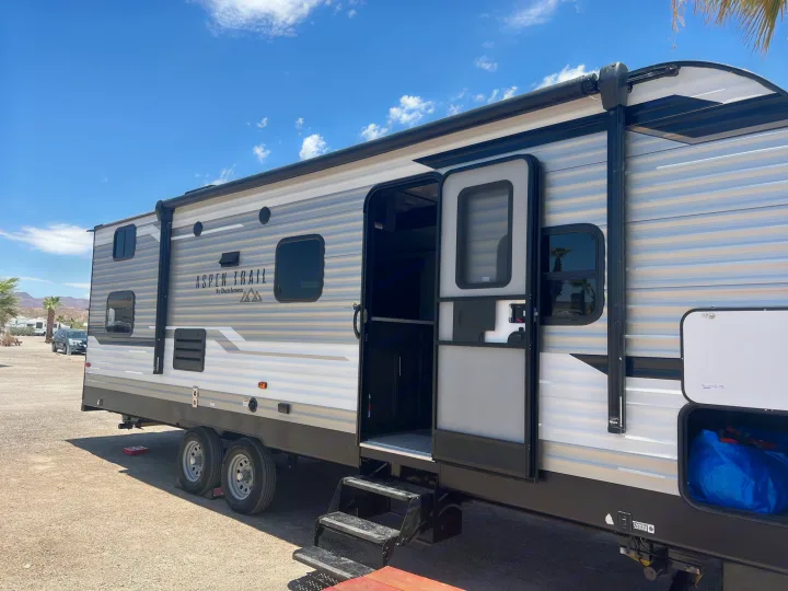 Spacious Aspen Trail travel trailer, an RV rental, with open door & steps at a sunny campground.. Aspen Trail Aspen Trail Trailer 2021