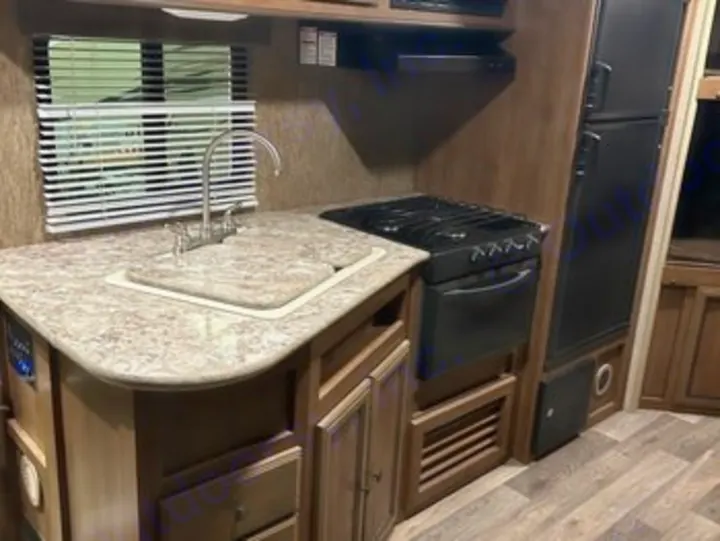 RV rental kitchen area, featuring a compact sink, stove, fridge, and cabinets. Ideal for travel.. Heartland RVs Sundance XLT 2016