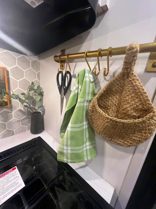 RV rental kitchen with organized essentials: green towel, scissors, and a basket hanging from a brass rod over the stovetop.. Jayco 224BHW 2024