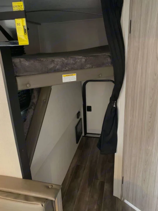 Cozy RV rental bunk beds with a privacy curtain, leading to a hallway with wood flooring and a door. Perfect camper space.. Keystone RV Passport SL 2021