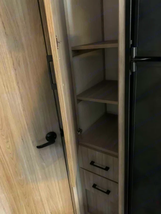 RV rental interior: Open pantry with wood shelves, drawers, and part of a refrigerator door for organized storage.. Keystone RV Passport SL 2021