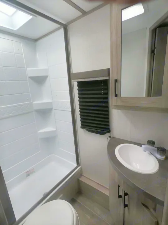 Inside an RV rental, this clean bathroom features a stand-up shower, toilet, and vanity with an oval sink.. Keystone RV Passport SL 2021