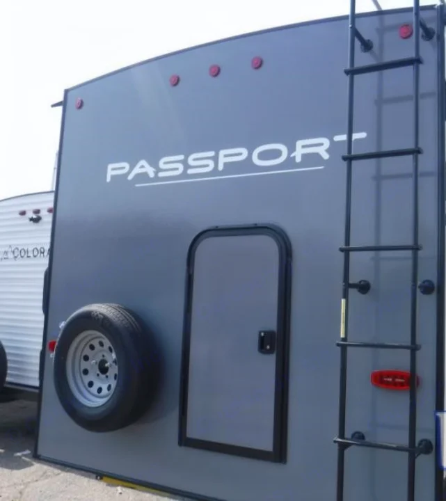 Gray RV rental's rear features a ladder, spare tire, and access door. The 'PASSPORT' brand is visible on the travel trailer.. Keystone RV Passport SL 2021