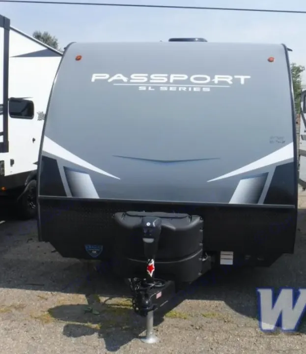 Front view of a gray Keystone Passport SL Series travel trailer, an ideal RV rental. Features visible propane tanks and modern graphics.. Keystone RV Passport SL 2021