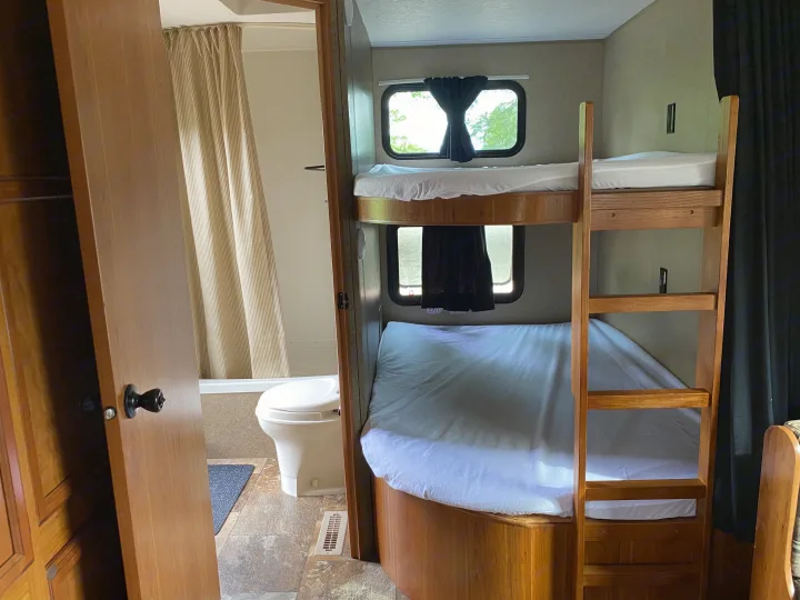 This RV rental interior features bunk beds on the right and a compact bathroom with a toilet and shower curtain on the left.. Starcraft Ar-One MAXX 2016