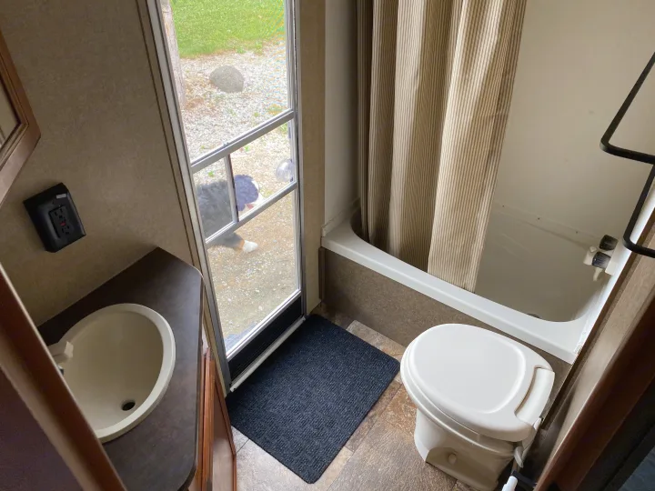 RV rental bathroom features: compact sink, toilet, tub with curtain. A dog curiously peeks through the screen door.. Starcraft Ar-One MAXX 2016