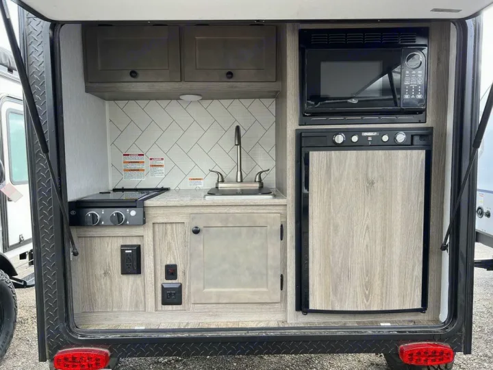 Outdoor kitchen in an RV rental featuring a stove, sink, microwave, and fridge, perfect for camping convenience.. Sunset Park RV SunRay 2023