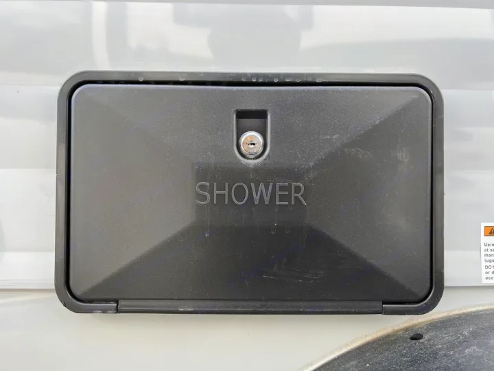 Black outdoor shower access panel with keyhole on an RV rental.. Sunset Park RV SunRay 2023