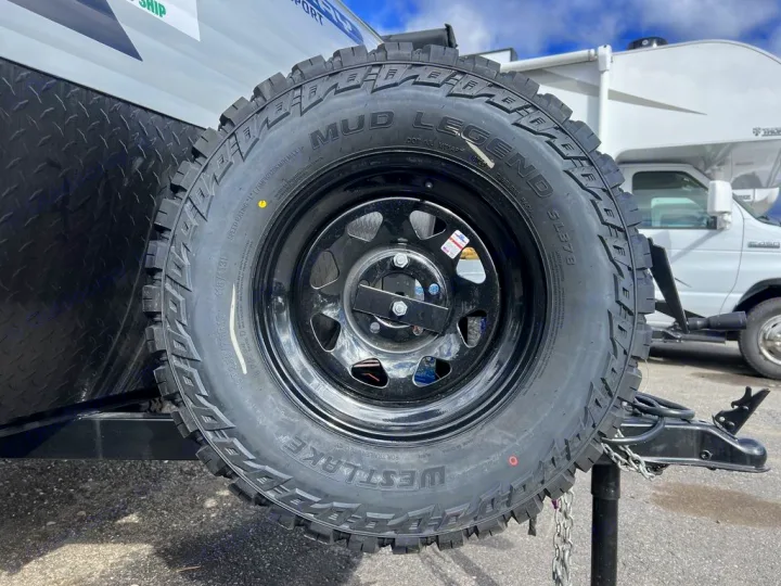 A new Westlake Mud Legend spare tire is mounted on the front of an RV rental trailer, with a white camper van behind.. Sunset Park RV SunRay 2023