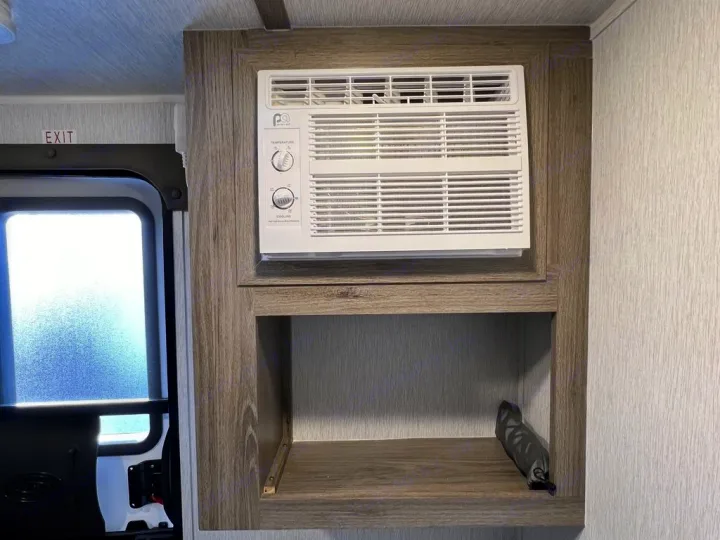 RV rental interior: Integrated AC unit for cooling comfort, storage shelf, and exit door visible.. Sunset Park RV SunRay 2023