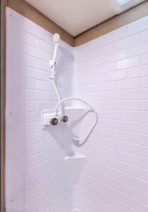 Compact white shower in an RV rental, featuring a handheld showerhead, controls, and corner shelf. Ideal for road trips.. Coachmen Catalina 2022