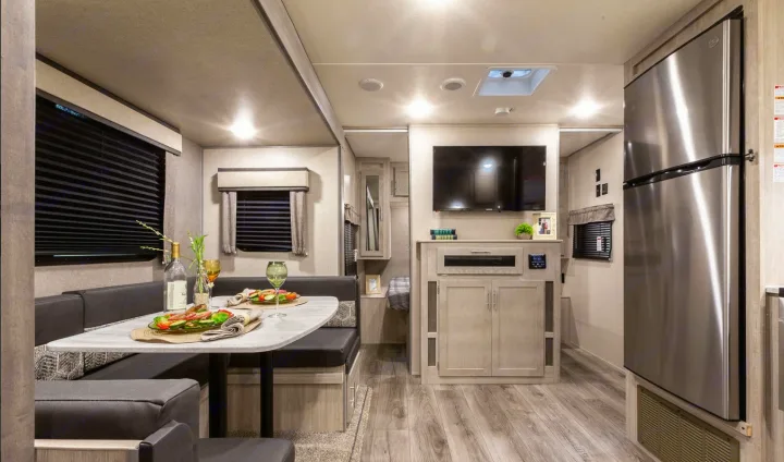 Bright RV rental interior featuring a comfortable dining booth, entertainment center with TV, and large refrigerator.. Coachmen Catalina 2022