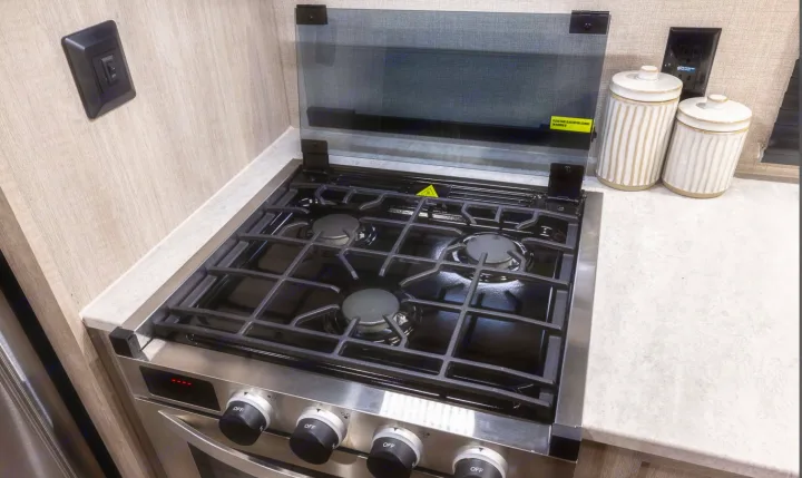RV rental kitchen showing a modern 3-burner gas range, protective glass cover, and light countertops for a functional space.. Coachmen Catalina 2022