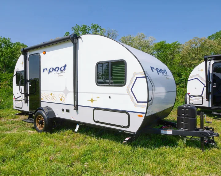 White R-pod travel trailer for RV rental, parked in a grassy field under a blue sky, ideal for camping adventures.. Forest River R-Pod 190 2024