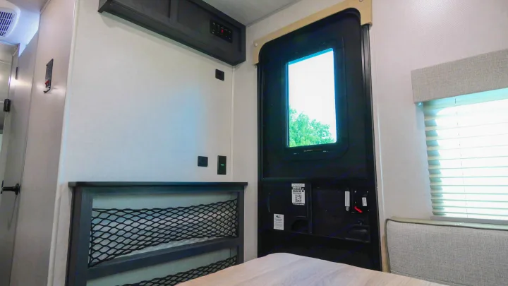 An RV rental's interior reveals a bed with mesh storage, a door with window view, and overhead controls.. Forest River R-Pod 190 2024