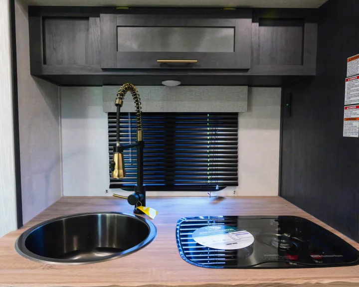 Modern RV rental kitchen with dark cabinets, wood counter, black sink, and two-burner stove.. Forest River R-Pod 190 2024