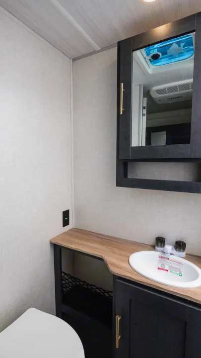 Modern RV rental bathroom features a wooden vanity with sink, toilet, and mirrored cabinet. Walls are light-textured.. Forest River R-Pod 190 2024