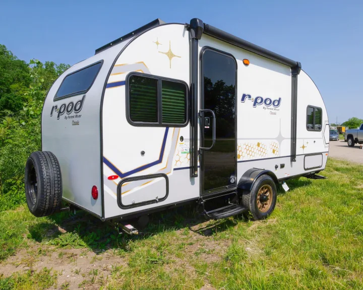 Explore the open road with this white r-pod travel trailer, a perfect RV rental, featuring a spare tire and jack stand.. Forest River R-Pod 190 2024