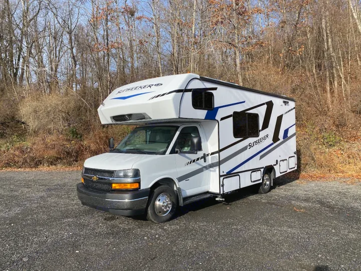 This white Sunseeker RV rental is parked on gravel, backed by bare trees, ready for your next adventure.. Forest River Sunseeker 2025