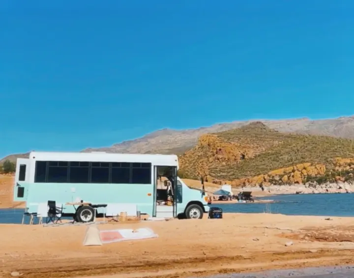 Light blue bus conversion by a desert lake, mountains in background. An ideal spot for an rv rental outdoor escape.. Ford E450 1999