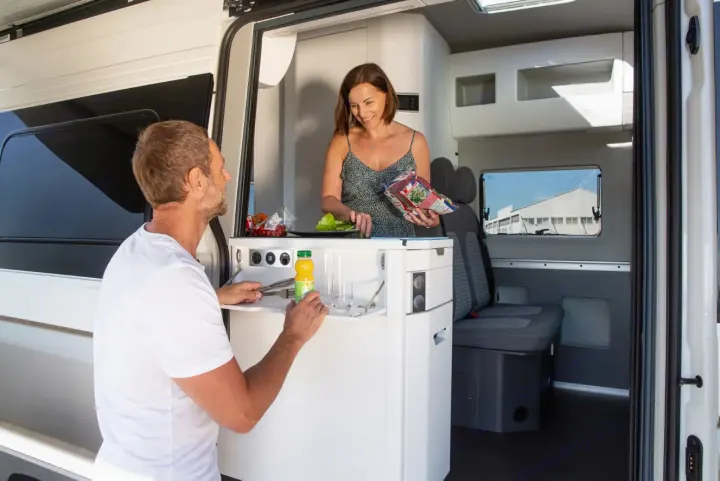 Man and woman preparing food in a compact, functional RV rental kitchen. Ideal for road trips.. Volkswagen Grand California 600 2023