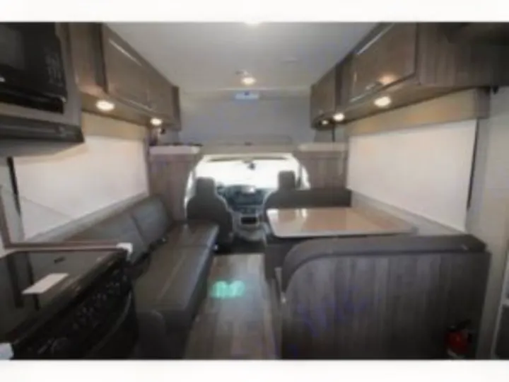 Explore this inviting RV rental interior: kitchen with stove, sofa, and dining booth. View towards the driver's area.. Winnebago Minnie Winnie 2024