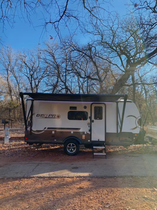 A white & brown GEO PRO RV rental is parked at a leafy campsite under bare trees & a clear sky, ready for adventure.. Forest River Rockwood Geo Pro 2024