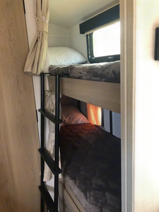 Cozy bunk beds with a ladder, window, and curtains inside an RV rental, offering a comfortable and compact sleeping area.. Forest River Rockwood Geo Pro 2024