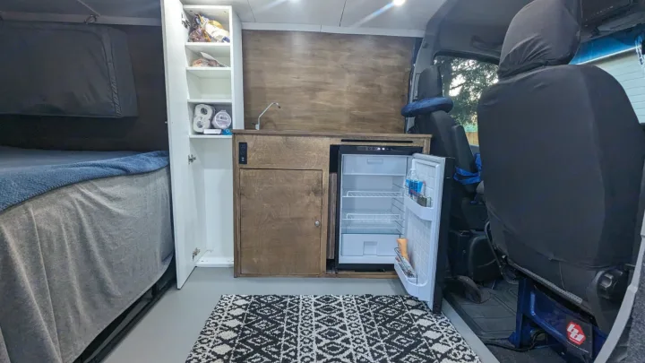 Inside a comfortable rv rental: a full bed, compact kitchen with sink, and open fridge in this modern campervan conversion.. Dodge Sprinter 2007