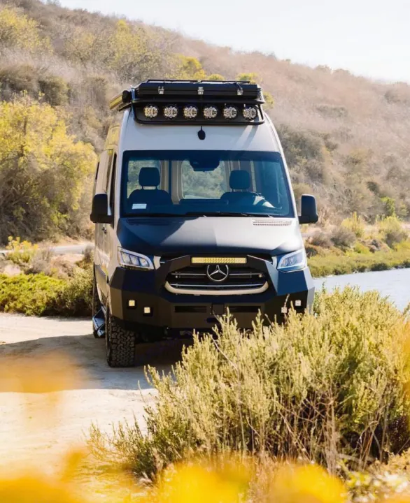 Customized black & light-colored Mercedes Sprinter van, an ideal rv rental. It features off-road tires & bumper, parked on a dirt path.. Vanspeed Mercedes Sprinter 2021