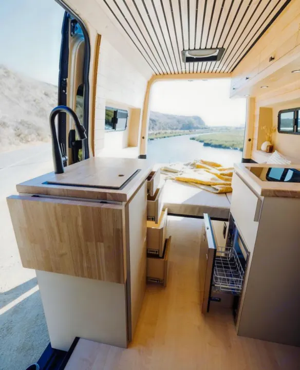 This RV rental offers a sleek camper van interior with a compact kitchen & cozy bed, opening to a scenic river view.. Vanspeed Mercedes Sprinter 2021