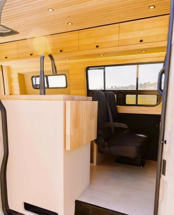 Spacious RV rental interior featuring a modern kitchen area with sink, light wood accents, and comfortable passenger seating.. Vanspeed Mercedes Sprinter 2021