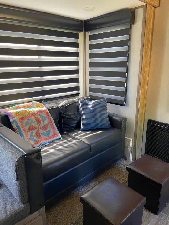 Cozy RV rental living space with a comfy sofa, colorful quilt, and modern zebra blinds offering comfort on your journey.. Forest River Cherokee Arctic Wolf 2021