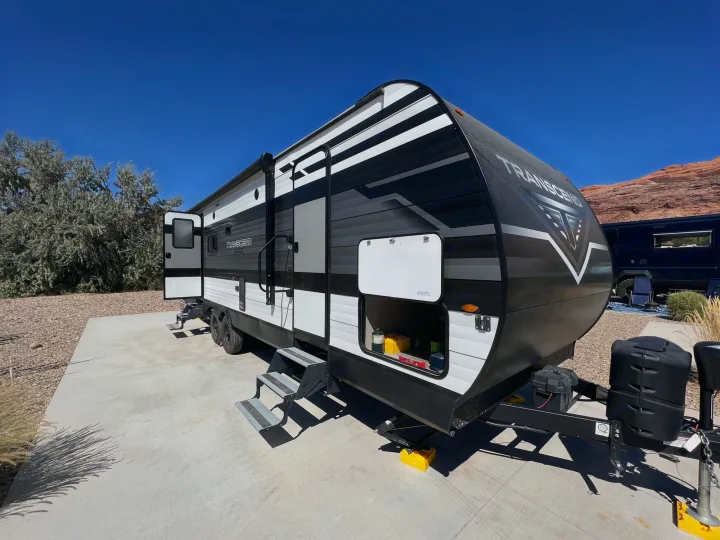 Black/white Transcend travel trailer (RV rental) at a sunny desert campsite. Steps are down, ready for outdoor adventure.. Grand Design Transcend Xplor 265BH 2022