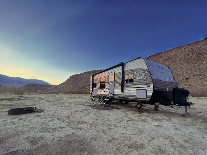 An RV rental parked at a peaceful desert campsite with distant snowy mountains under a clear sky. Perfect for nature lovers.. Jayco Jay Flight SLX Rocky Mountain Edition 2021