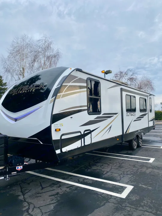 Modern white travel trailer, an ideal RV rental. Parked in lot under cloudy sky, ready for your next adventure.. Keystone RV Outback Ultra-Lite 2022