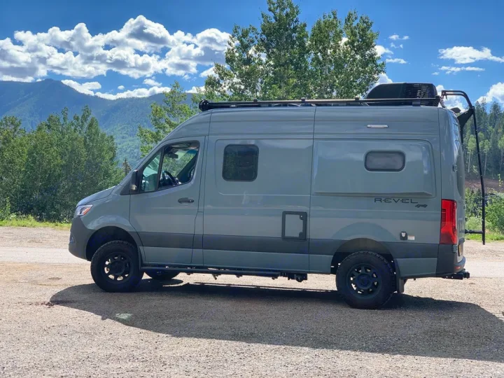 Gray Winnebago Revel 4x4 rv rental parked on gravel with mountains and trees under a blue sky.. Winnebago Revel 2022