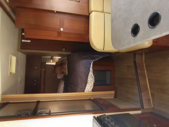 Inside an RV rental: a compact living space featuring a cozy bed, dining area with table and seats, and wood cabinets.. Forest River Forester 2018
