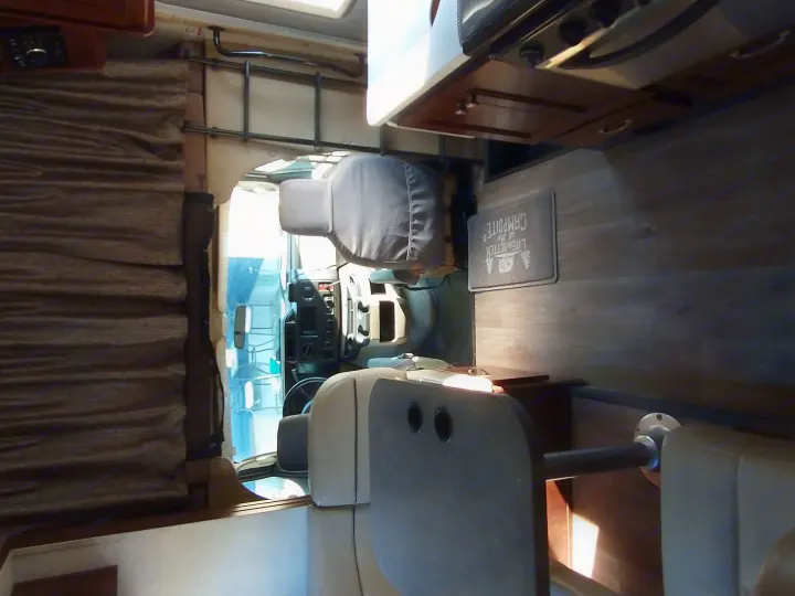 Inside a cozy RV rental: dining area with table, kitchen counter, and driver's cab, plus a "Campsite" floor mat.. Forest River Forester 2018
