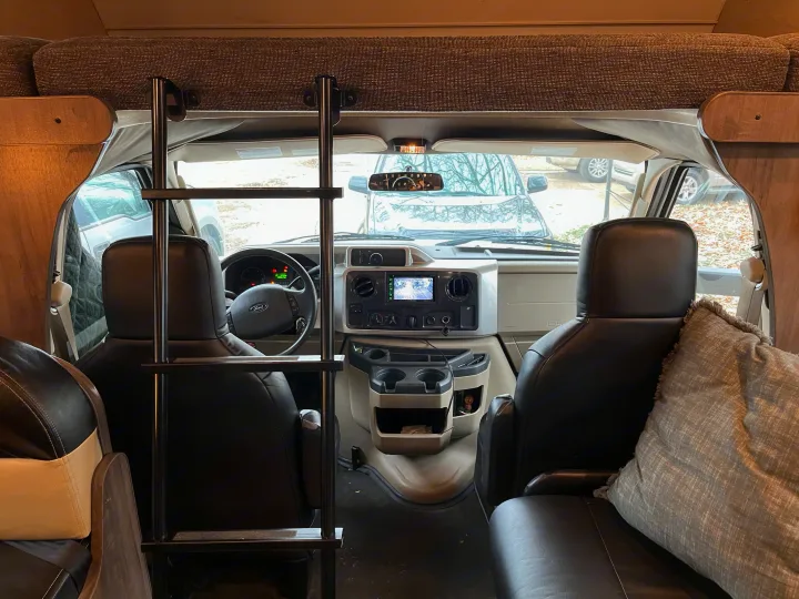 Step inside this RV rental! View of the front cab, Ford dashboard, comfy driver/passenger seats, and an overhead bunk with ladder.. Winnebago Spirit 2017