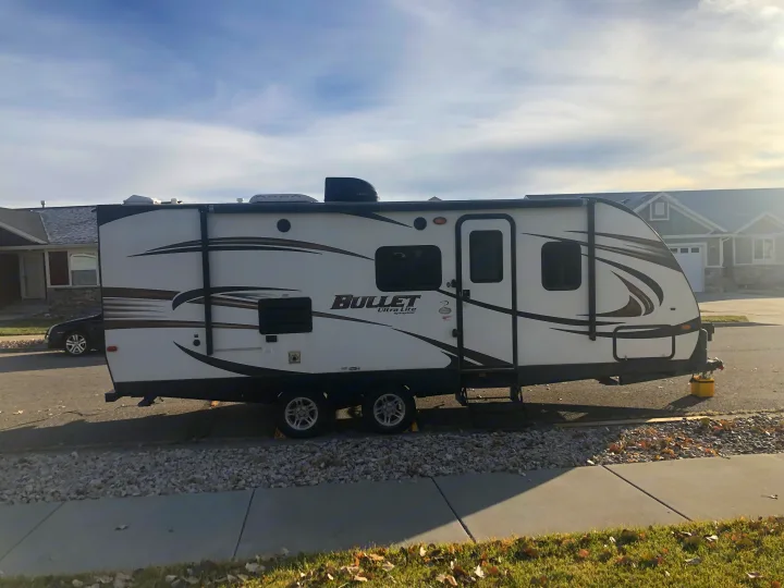 A white Bullet Ultra Lite travel trailer, ideal for an RV rental, prominently parked on a sunny street.. Keystone RV Bullet Ultra Lite 2015