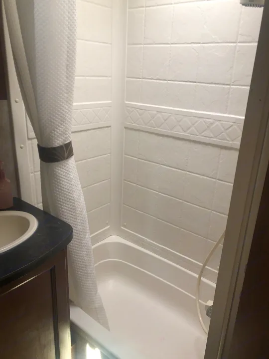 This RV rental's compact bathroom features a white textured shower, a small tub, and a sink vanity, with a tied-back shower curtain.. Keystone RV Bullet Ultra Lite 2015