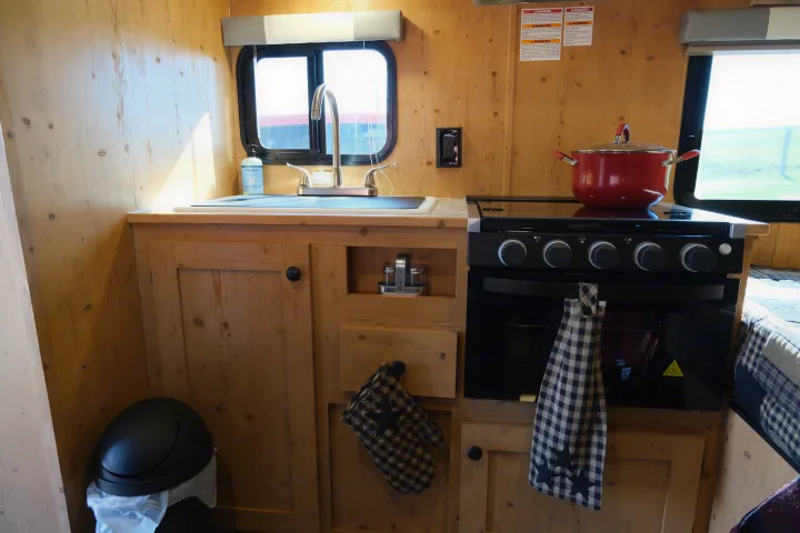 RV rental kitchen: compact, wood-paneled space with a sink, modern electric stove, and cozy cabin feel, ideal for travel.. Sunray Sunlite 16BH 2023