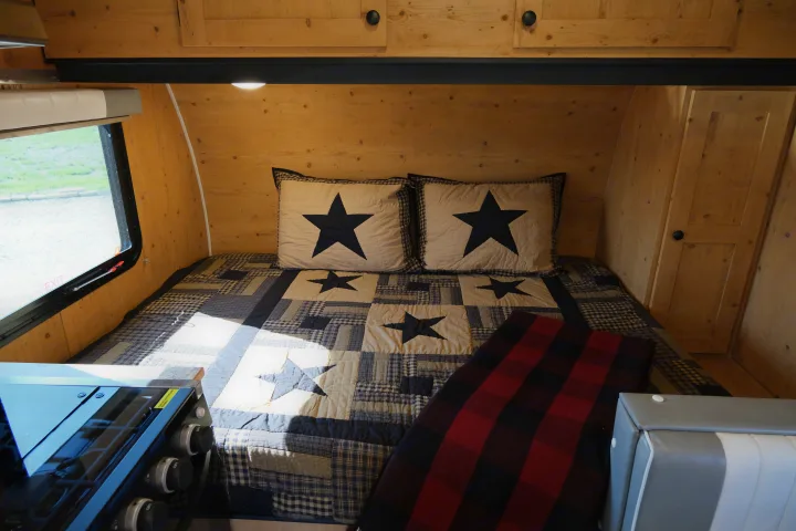 Inside a cozy **rv rental** featuring a bed with star-patterned quilt, wooden walls, and a compact stove.. Sunray Sunlite 16BH 2023